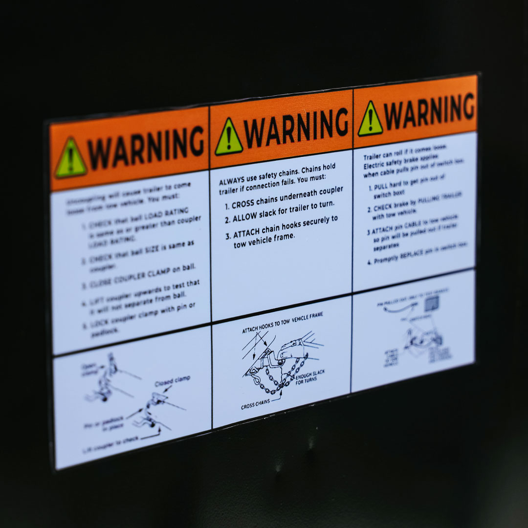 DOT warning label on a restroom trailer showing safety instructions for hitch coupling, safety chains, and breakaway brake system